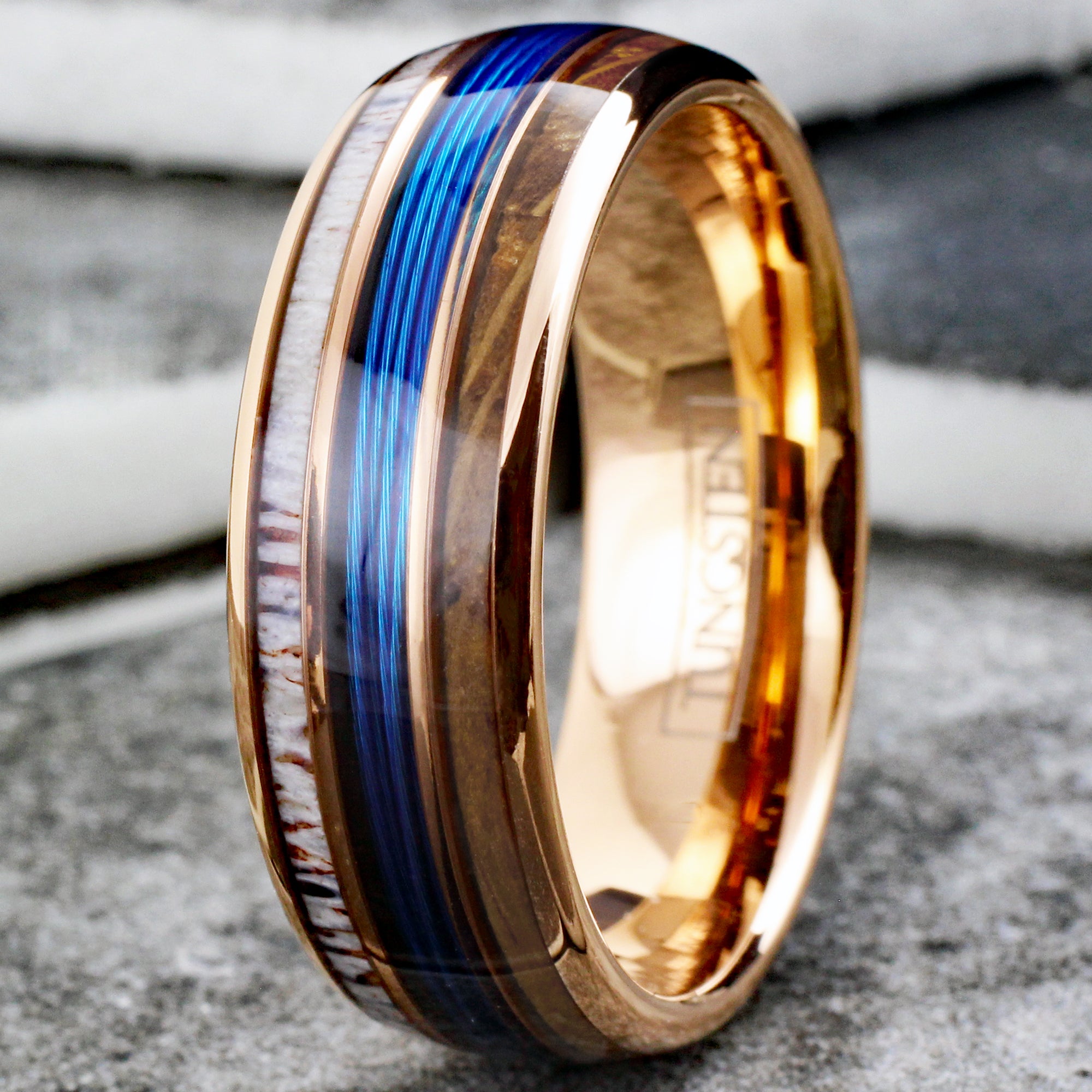 https://www.kingscrossjewelry.com/cdn/shop/files/Rose-gold-tungsten-carbide-low-dome-band-ring-with-blue-fishing-line-between-whiskey-oak-barrel-wood-and-deer-antler-inlays-tungsten-rings-c-tile-photo.jpg?v=1706673365
